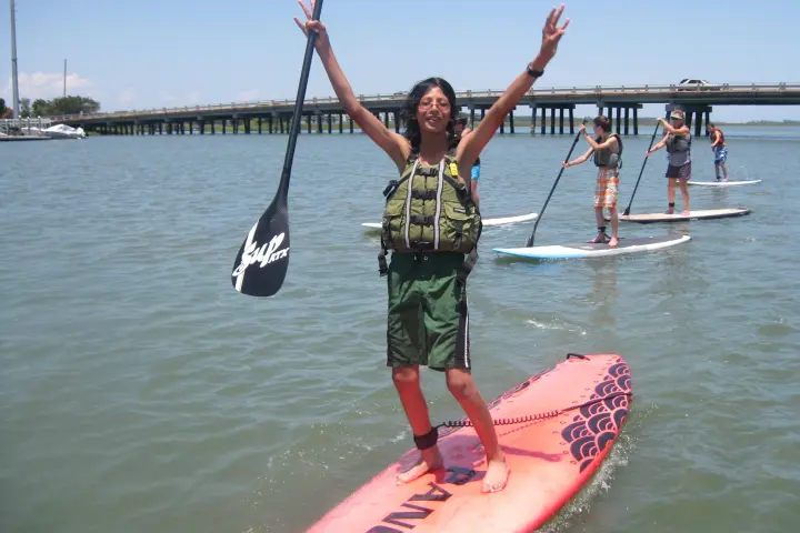 kid with his hand in the air on paddle board