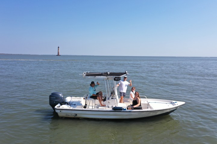 Small boat with four people on calm water, distant lighthouse in background.